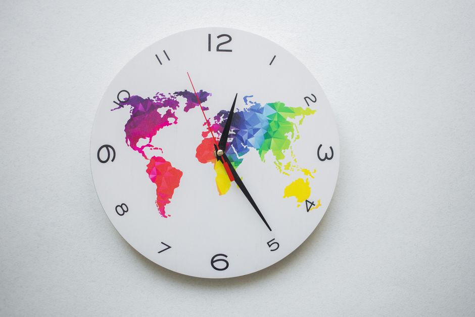 Round wall clock with colorful world map design and black hands, symbolizing global time.